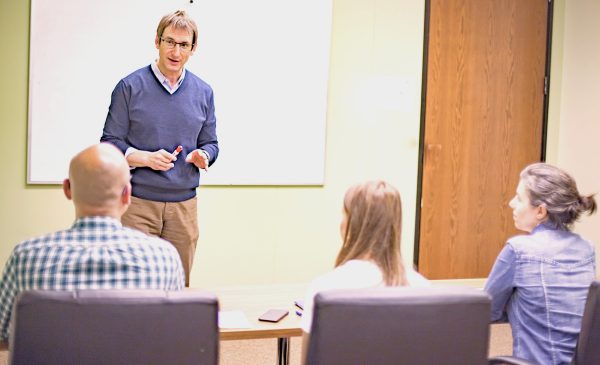 Darren Packard teaching a small group in a classroom, standing in front of a whiteboard