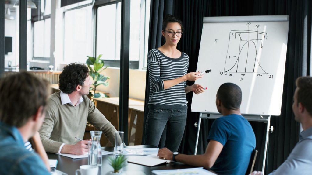 Confident professional woman presenting to colleagues during a workplace meeting, demonstrating clear English communication skills.