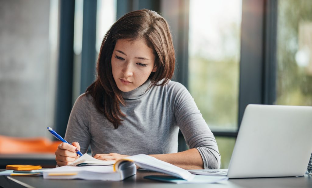 Adult English learner studying pronunciation and accent training materials at a desk with a notebook and laptop.
