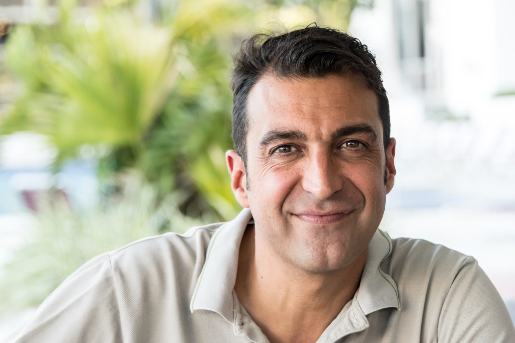 Smiling Middle Eastern man sitting outdoors, representing an Arabic speaker improving English pronunciation and confidence.