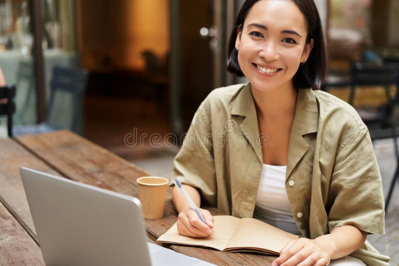 A young Korean woman studying at a café with a laptop and notebook, representing Korean accent reduction practice and online English learning.